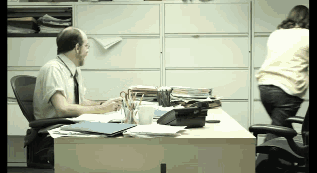 a man sits at a desk with a phone and a cup of coffee on it