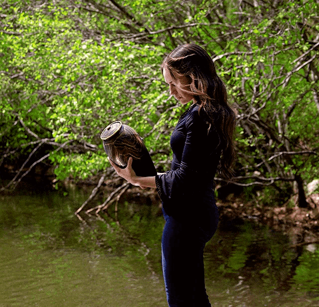 a woman in a black shirt is holding a jar in her hands