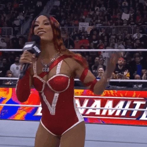 a woman in a red and white wrestling outfit is holding a microphone in front of a sign that says dynamite