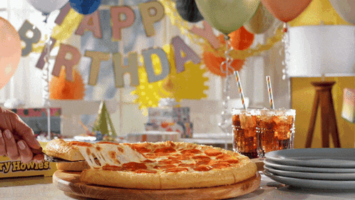 a pizza with a slice taken out of it sits on a table in front of a happy birthday banner