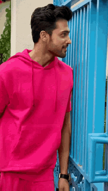 a man wearing a pink hoodie stands in front of a blue gate