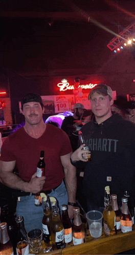 a man in a carhartt shirt is standing next to a man holding a beer