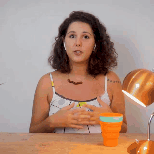 a woman sitting at a table with her hands up and a cup in front of her