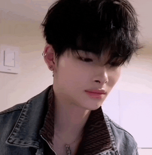 a close up of a young man wearing a denim jacket and a necklace with a cross .