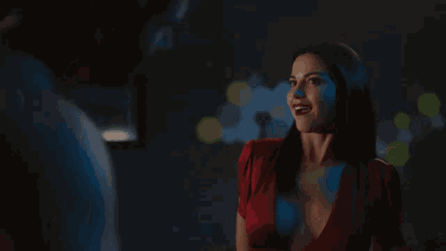 a woman in a red dress is standing next to a man in a dark room and smiling .