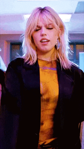 a woman wearing a black jacket and a yellow shirt is standing in a room with her eyes closed .
