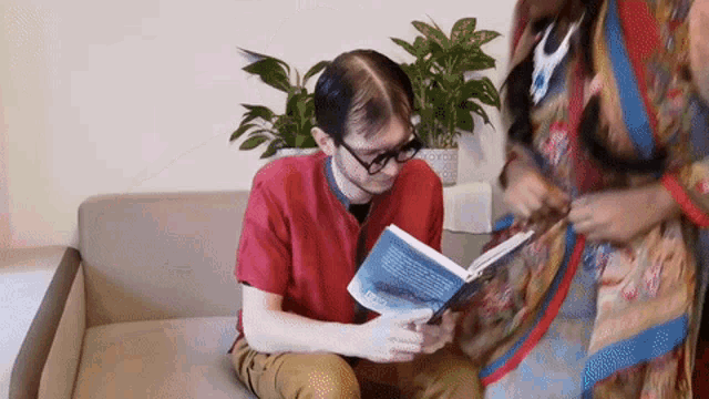 a man is reading a book while sitting on a couch .