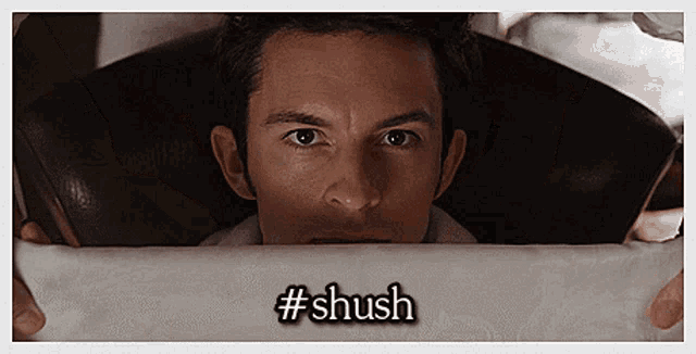 a man peeking out from behind a piece of paper with the hashtag #shush