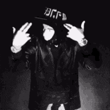 a man wearing a black hat and a leather jacket is making a peace sign with his hands .