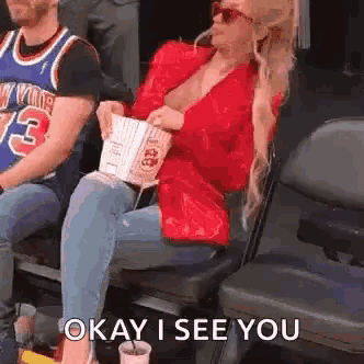 a woman is sitting in a stadium holding a bag of popcorn and a cup of soda .