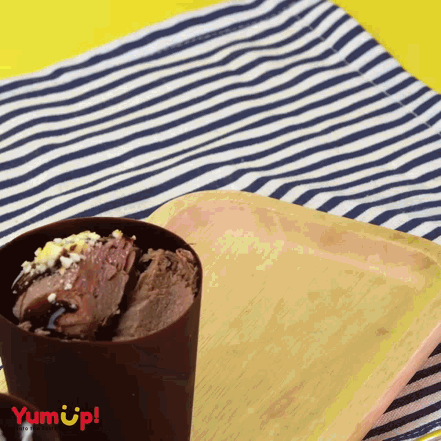 a cup of chocolate ice cream sits on a striped napkin next to a wooden tray