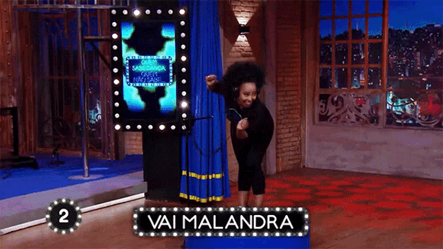 a woman dancing in front of a sign that says " vai malandra "