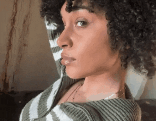 a woman with curly hair is wearing a striped sweater and looking at the camera .