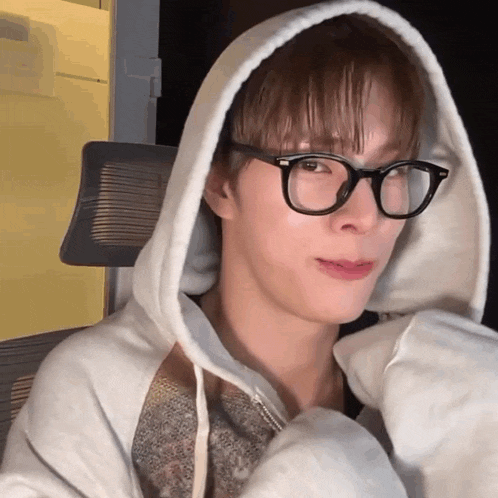 a young man wearing glasses and a white hoodie looks at the camera
