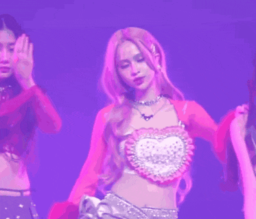a woman in a pink top and silver skirt is standing on a stage in front of a purple background .