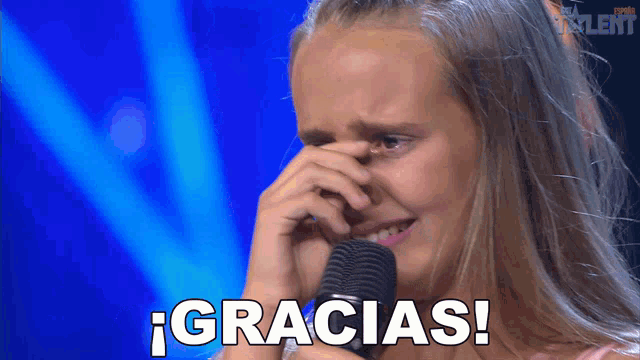 a girl crying in front of a microphone with the word gracias written on the screen