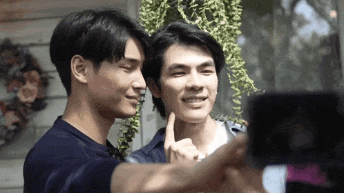 two men are taking a selfie with a cell phone .