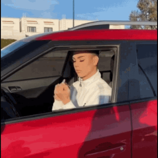 a man is sitting in a red car applying makeup