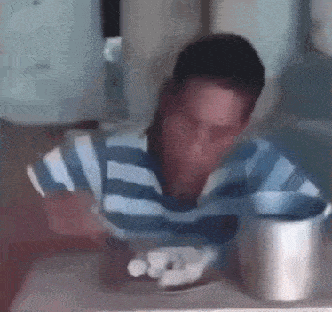 a man in a blue and white striped shirt is sitting at a table with a cup of coffee in front of him .