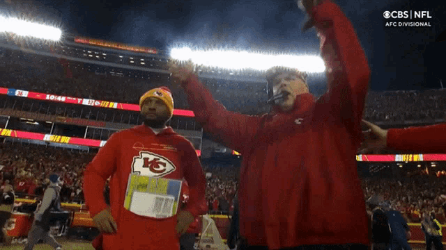 a man in a chiefs sweatshirt holds up his arms in the air