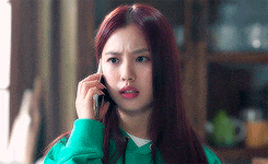 a young woman is talking on a cell phone while wearing a green hoodie .