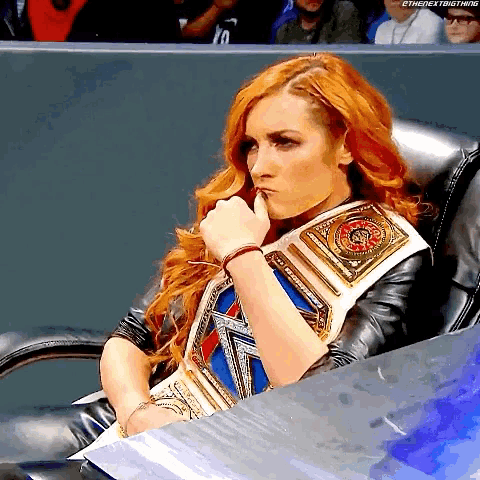 a woman with red hair is sitting in a chair wearing a wrestling belt .