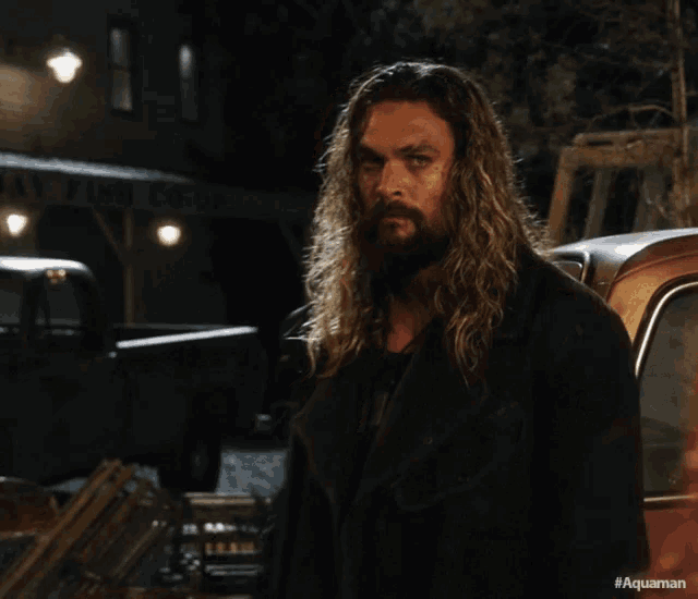 a man with long hair and a beard is standing next to a car with the hashtag #aquaman on the bottom