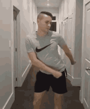 a man is dancing in a hallway in a nike shirt and shorts .
