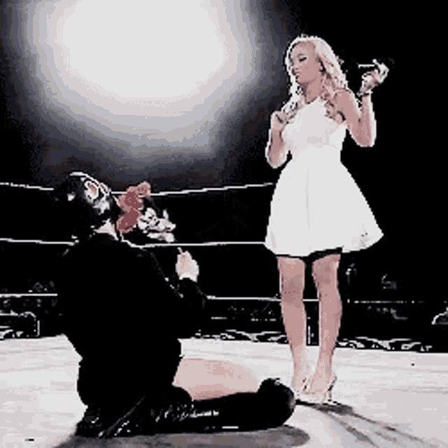 a woman in a white dress is kneeling down in front of a man in a black mask .