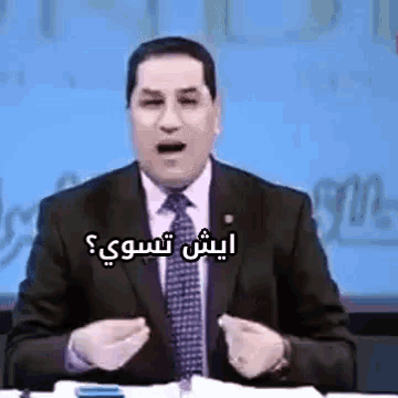 a man in a suit and tie is sitting at a table with his mouth open and talking in arabic .