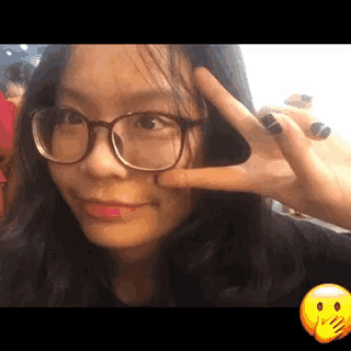 a girl wearing glasses is giving a peace sign