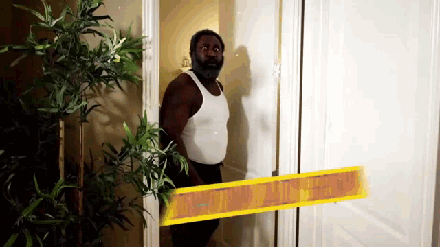 a man in a white tank top is standing in front of a door that has a yellow tape on it