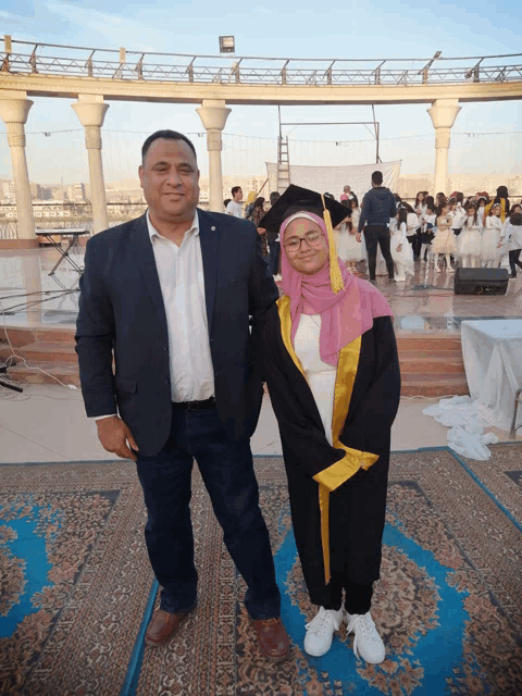 a man in a suit stands next to a girl in a graduation gown
