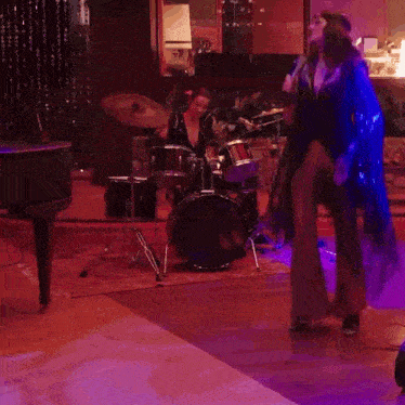 a woman sings into a microphone while a man plays drums