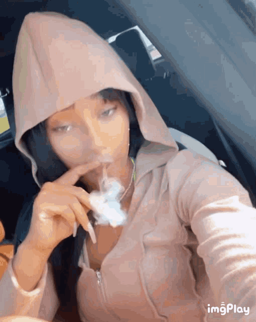 a girl in a hoodie is smoking a cigarette in a car .