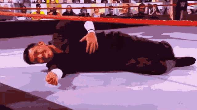 a man laying on the ground in a wrestling ring with a crowd watching