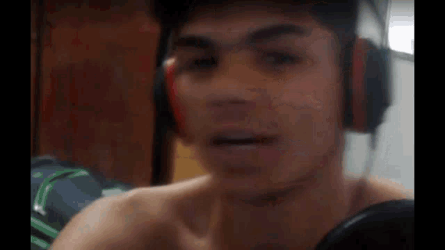 a shirtless young man wearing headphones and a hat is talking into a microphone .