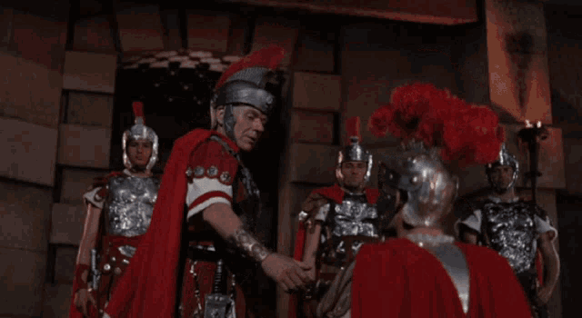 a man in a red cape shakes hands with a man in armor