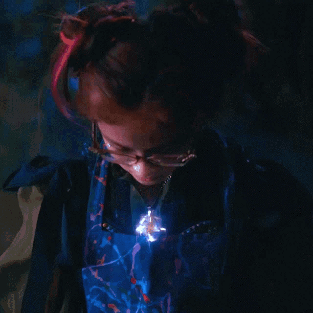 a woman wearing glasses and a necklace has a blue light shining on her chest