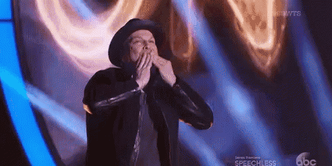 a man in a hat is blowing a kiss on a stage