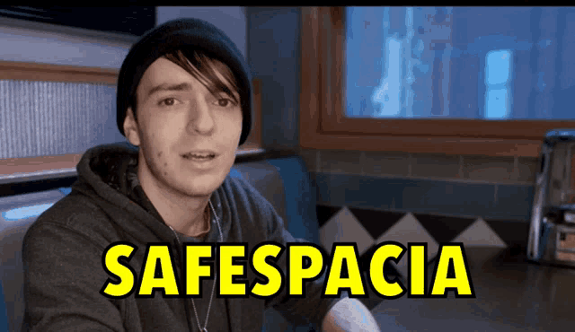 a man in a black hat sits in a diner booth with the words safespacioa written in yellow