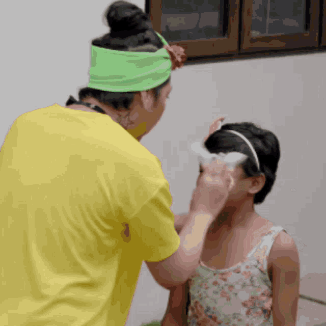a woman wearing a green headband is applying makeup to a little girl 's face
