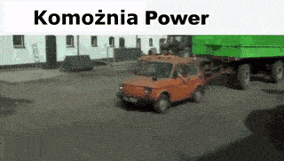 a car is driving past a green dump truck with the words komodnia power written above it