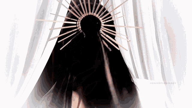 a woman wearing a black cape and a gold crown stands in front of a white curtain