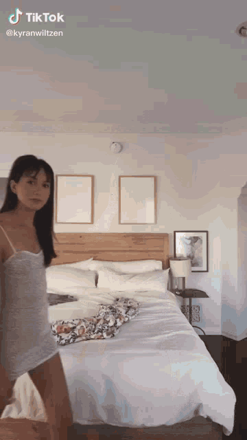 a woman in a white dress is standing in front of a bed