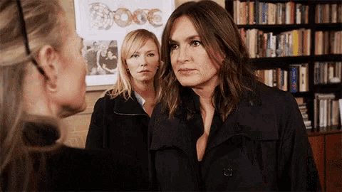 three women standing in front of a bookshelf with a picture of donuts on the wall