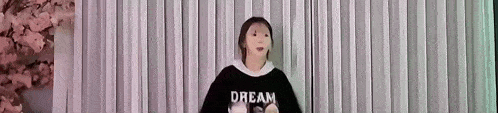 a woman wearing a black sweatshirt with the word dream on it is standing in front of a white curtain .