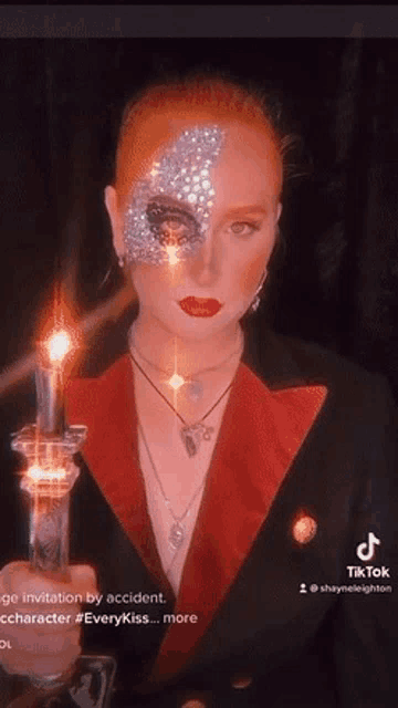 a woman with red hair and rhinestones on her face is holding a candle in her hand .