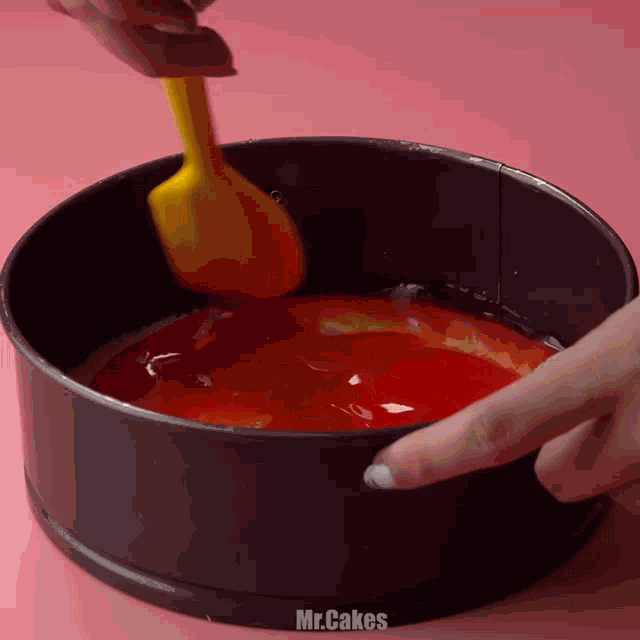 a person is using a yellow spatula to stir a red liquid in a pan that says mr.cakes