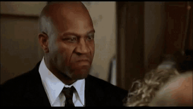 a man in a suit and tie is looking at another man in a room .